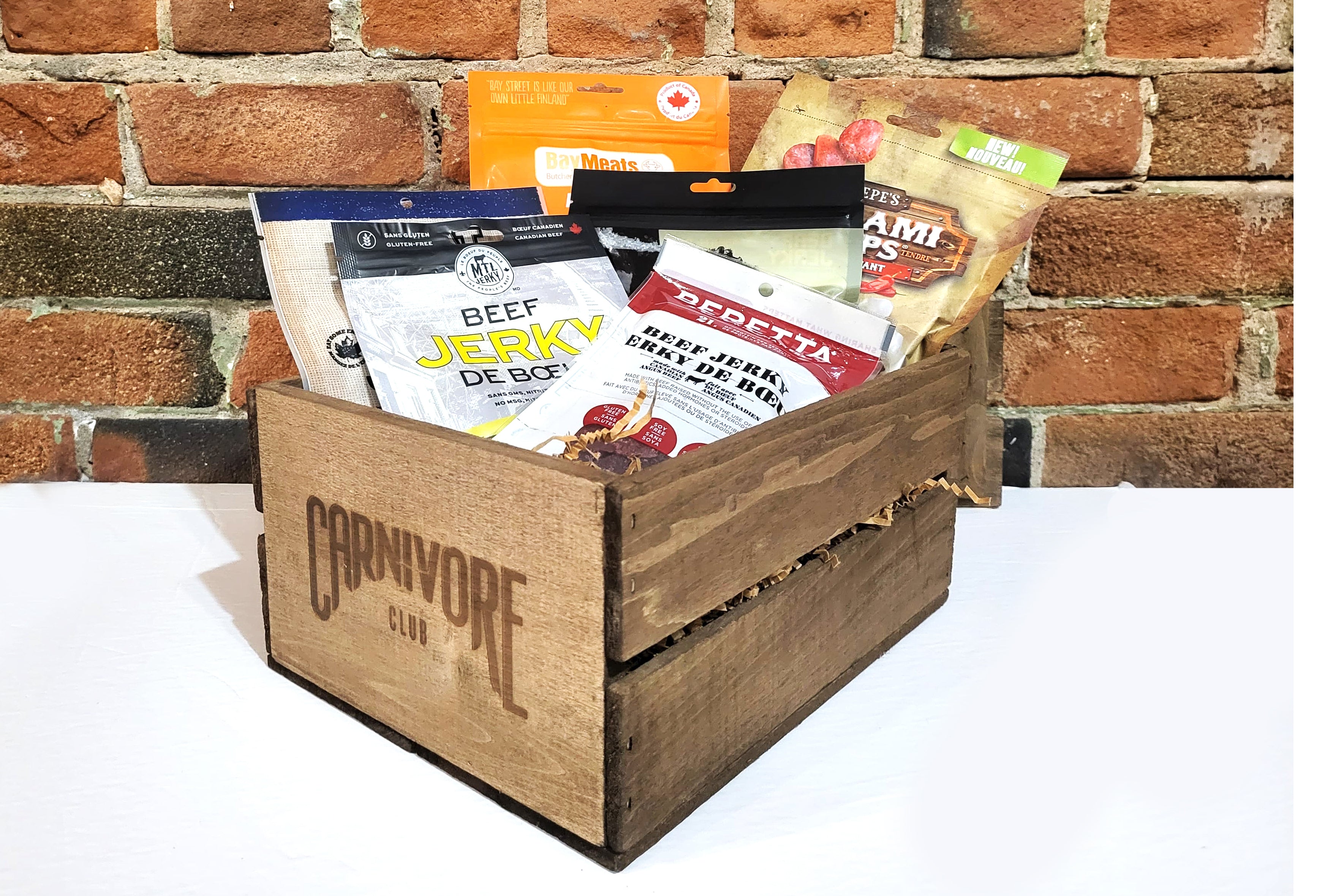 A wooden crate containing various packs of jerky, placed against a brick wall on a white surface.
